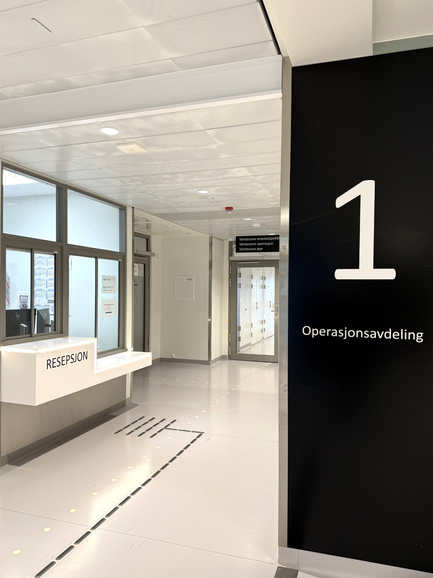 En lang korridor med glassdører, skilt og en resepsjon