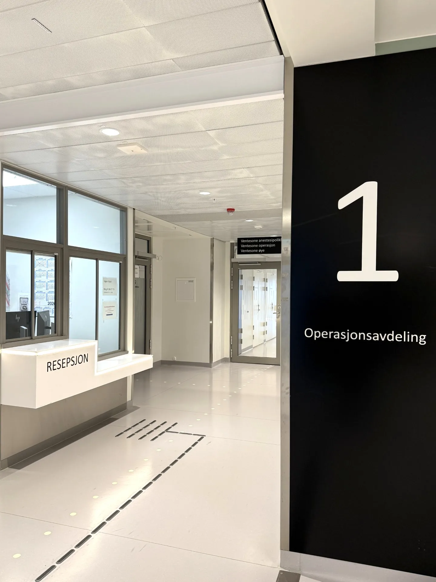 En lang korridor med glassdører, skilt og en resepsjon