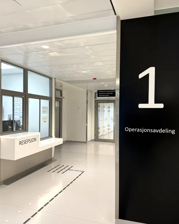 En lang korridor med glassdører, skilt og en resepsjon