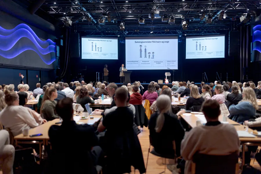 En gruppe mennesker som sitter i et rom med store skjermer