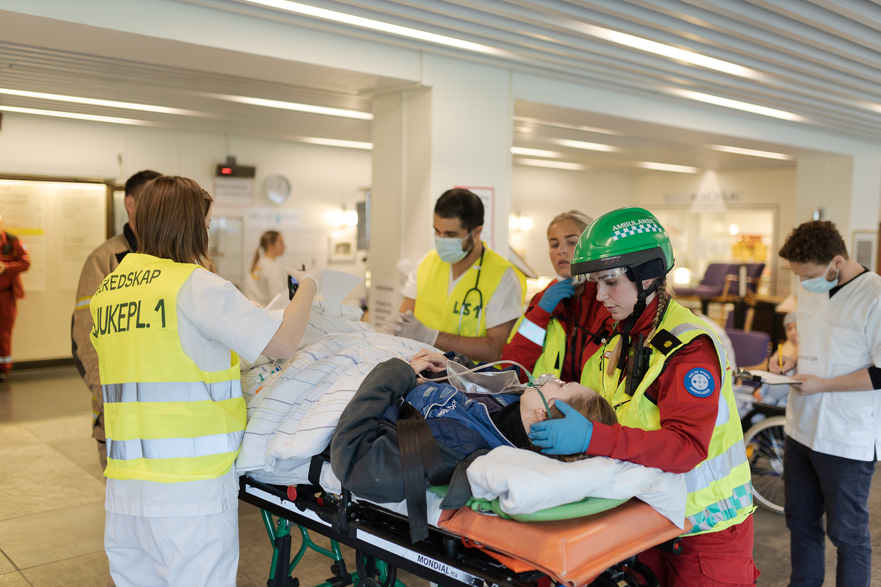 En gruppe mennesker i sikkerhetsvester som dytter en baby i en sykehusseng