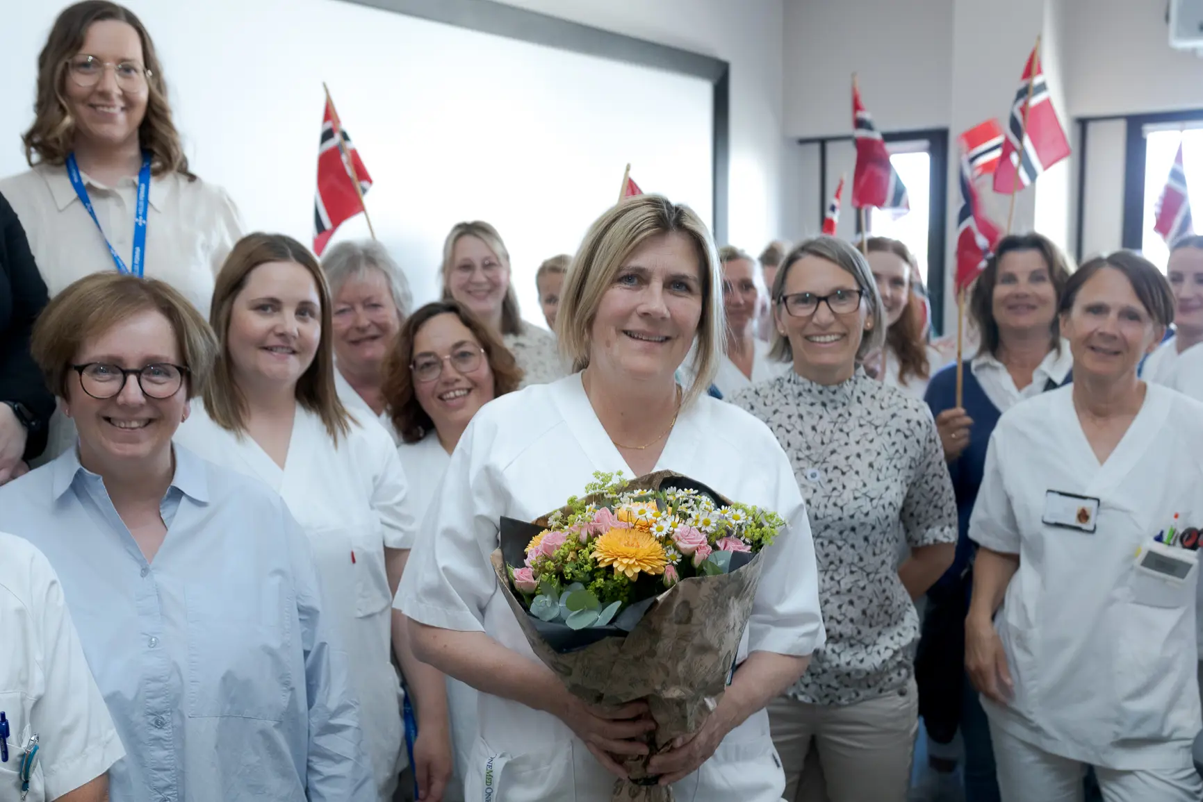 En gruppe kvinner i hvite laboratoriefrakker som holder blomster
