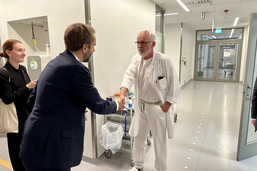 En mann i dress som håndhilser på en kvinne i hvit labfrakk
