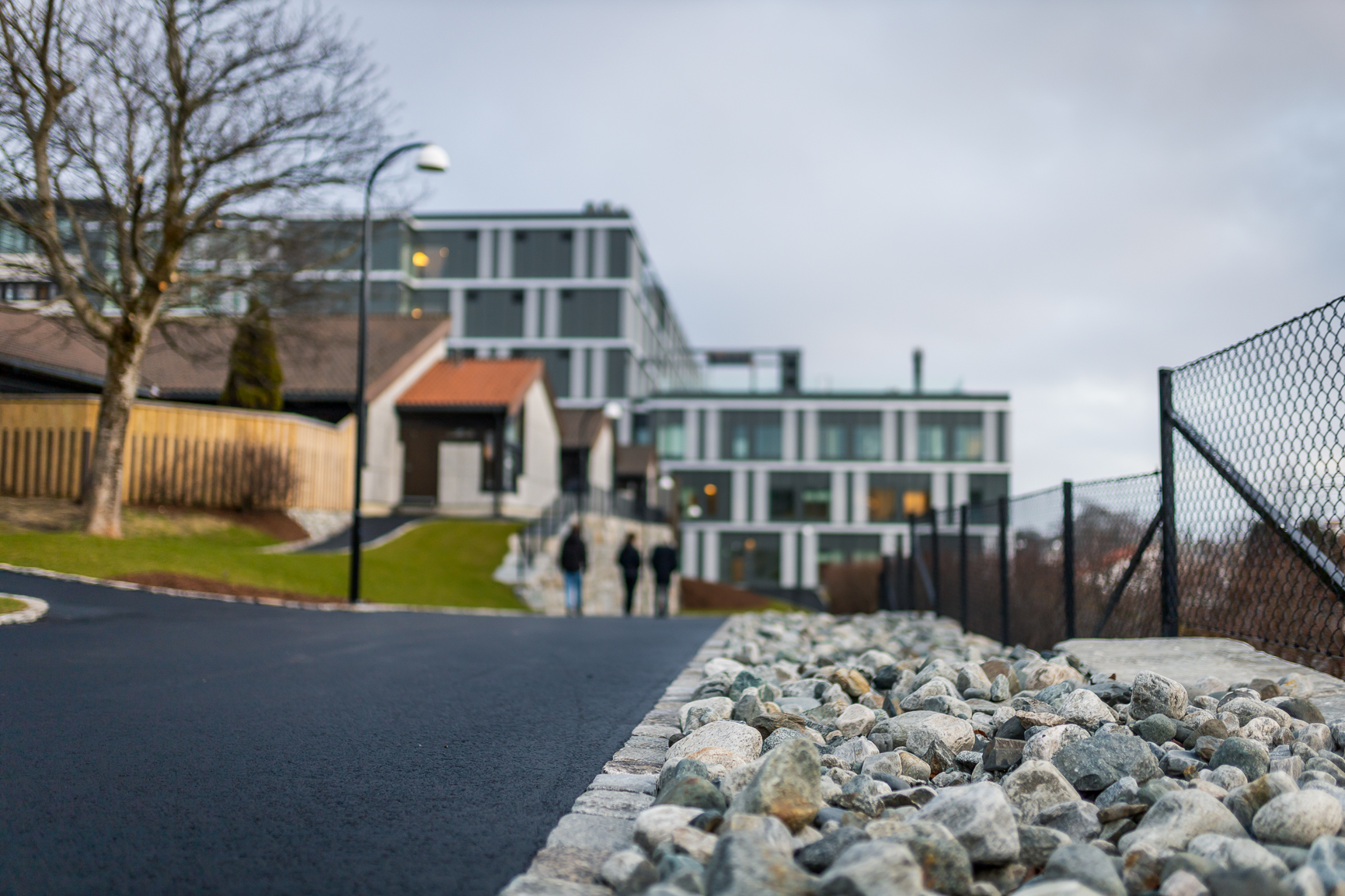 En gruppe mennesker som går på en vei ved siden av et gjerde og bygninger