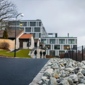 En gruppe mennesker som går på en vei ved siden av et gjerde og bygninger