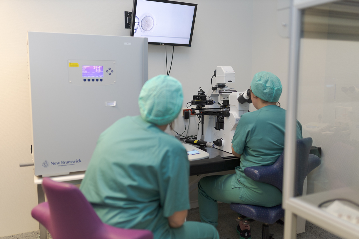 Et par personer i kirurgisk skrubb i et rom med labutstyr og skjerm