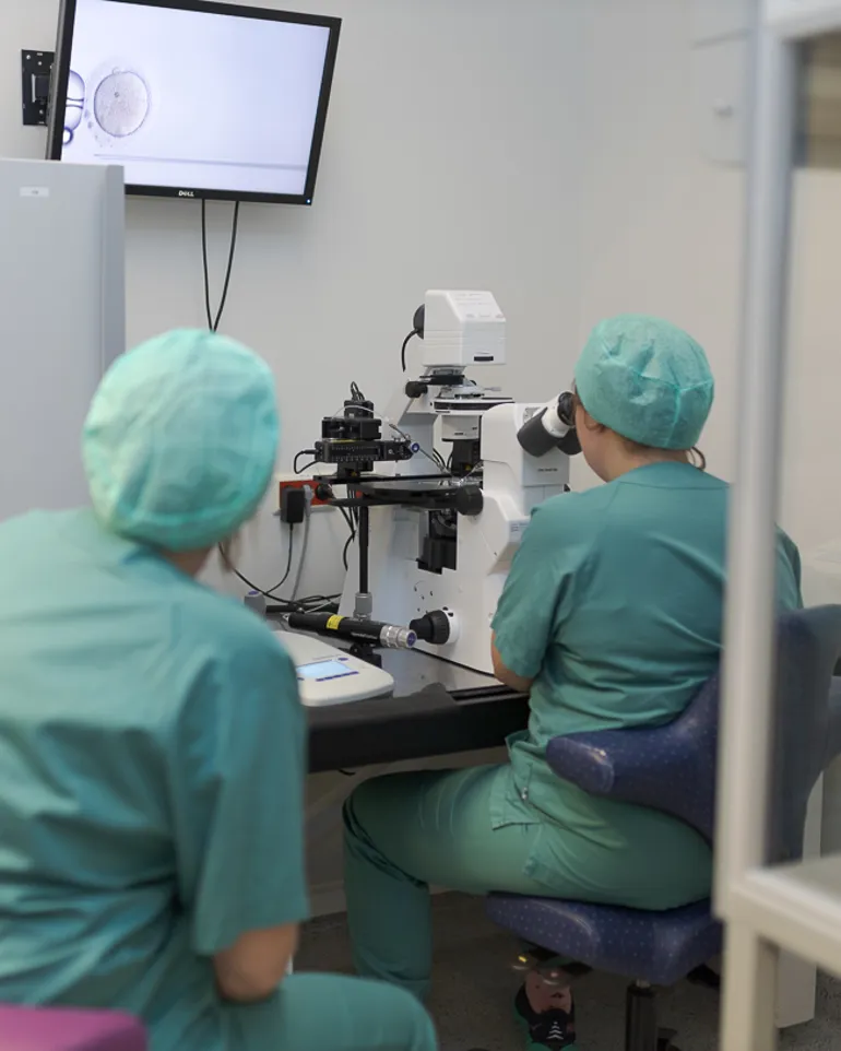 Et par personer i kirurgisk skrubb i et rom med labutstyr og skjerm