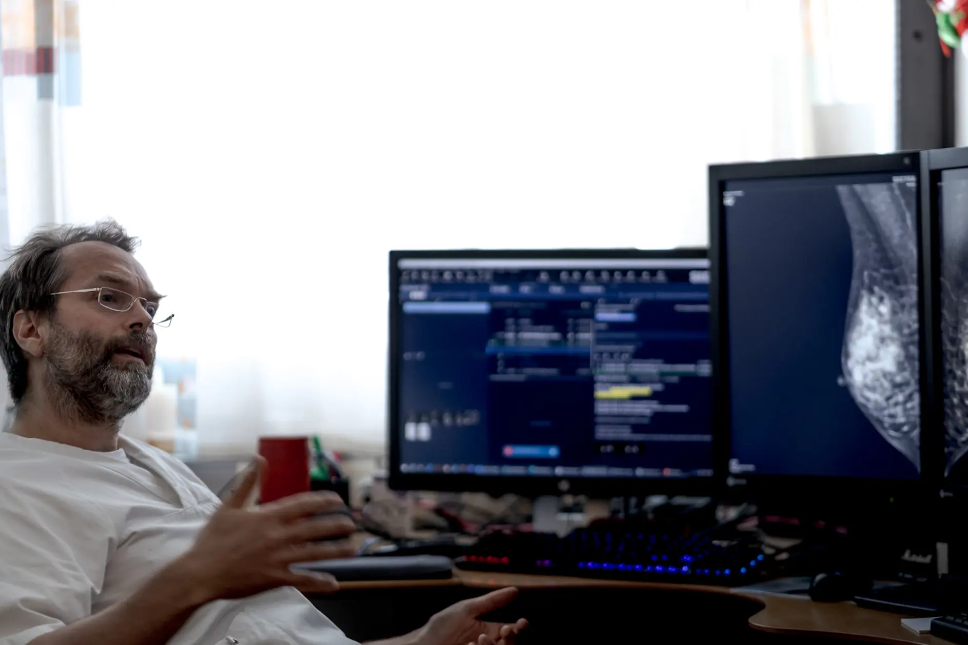 En mann som sitter ved et skrivebord med en datamaskin og et vindu