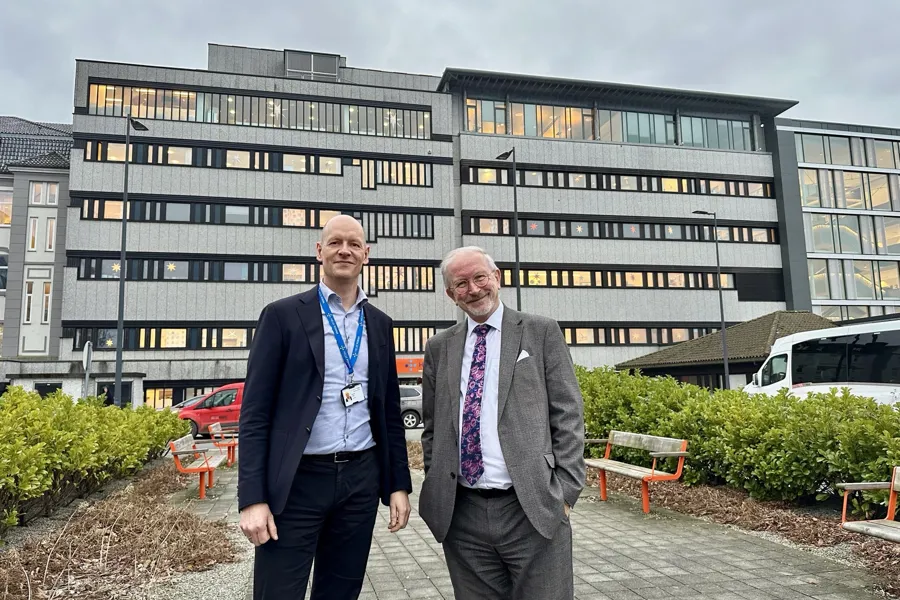 Et par menn som poserer for et bilde foran en bygning